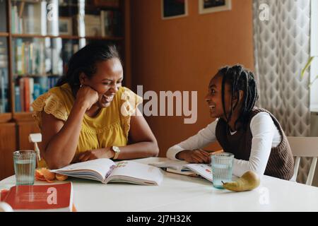 Happy daughter looking at mother laughing while sitting at table Stock Photo