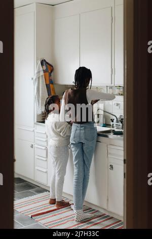 Rear view of sisters standing together in kitchen at home Stock Photo