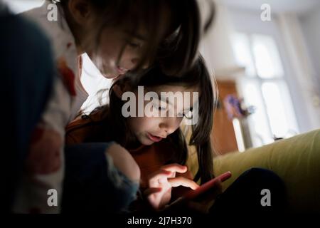 Girl using mobile phone sitting by sister at home Stock Photo