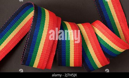 Rainbow spirally rolled textile tape close-up on dark background Stock Photo