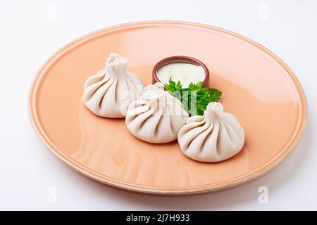 Khinkali - Traditional Georgian dumplings served with a sauce of sour cream & parsley. Isolated on white background. Stock Photo