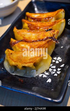Closeup of Japanese style fried gyoza (dumplings) in a black plate. Authentic shot at restaurant. Stock Photo