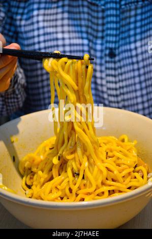 Chopsticks pick up ramen noodle from a white bowl. Authentic shot at restaurant. Stock Photo