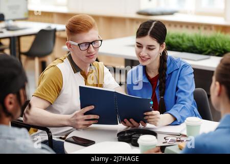 Vibrant shot of two smiling college students reading notes during group discussion in classroom Stock Photo