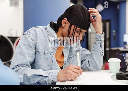 Vibrant side view portrait of young black man studying in college and taking notes Stock Photo