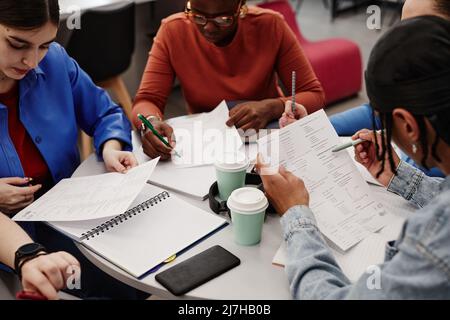 High angle view at diverse group of college students reading notes while working on project together Stock Photo