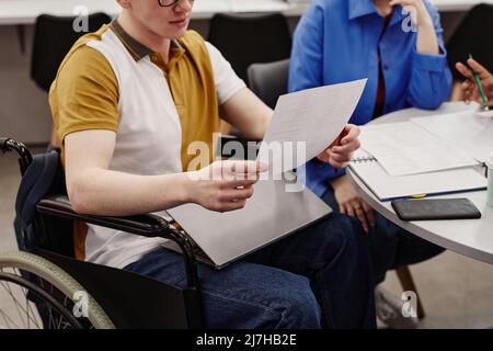Cropped shot of young college student in wheelchair reading notes while studying with group of friends, copy space Stock Photo