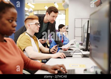 Vibrant portrait of male professor watching students using computers in college classroom Stock Photo