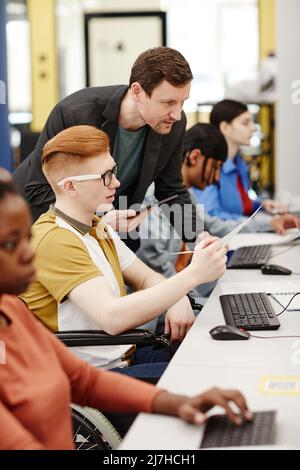 Vibrant vertical portrait of male teacher helping student using computer in college classroom Stock Photo
