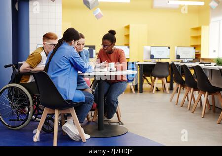 Vibrant full length shot of diverse group of students studying together at table in college lab, copy space Stock Photo