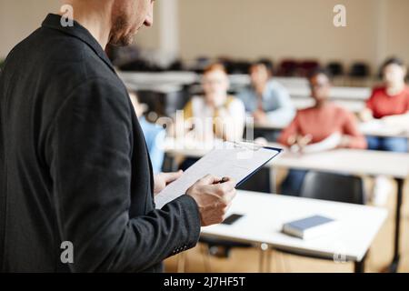 Closeup of male college professor checking notes while giving lecture to students in classroom, copy space Stock Photo