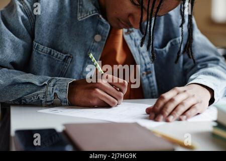 Closeup of black young man writing in notebook at desk in school classroom or in college Stock Photo