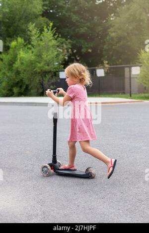 Child riding scooter. Little girl spending time outdoors in summer. Kid in a park on a sunny day. Stock Photo
