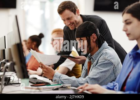 Side view portrait of male teacher helping African American student using computer in college classroom, copy space Stock Photo