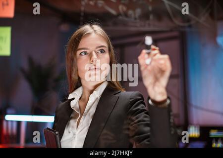 Close up portrait of female worker in formal wear writing on glass board at office room. Company worker analyzing financial report during business meeting. Stock Photo