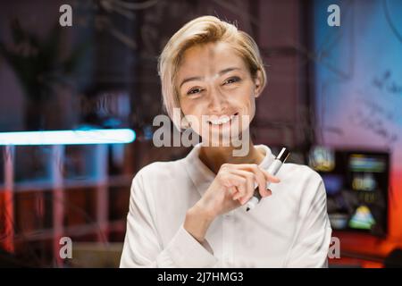 Close up of smiling likable blond Caucasian businesslady, working near glass board in office. View through the glass wall of female manager, developing new project strategy Stock Photo