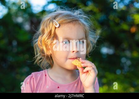 Small child having healthy snack on a sunny summer day outdoors. Little cute girl eating cookie in the park. Stock Photo