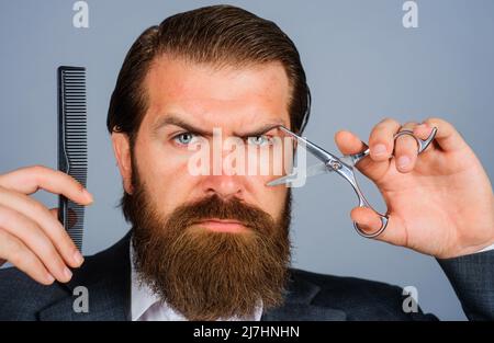 Barbershop advertising. Bearded man with scissors and comb. Male hairdresser with barber tools. Stock Photo