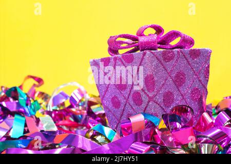 Wrapped decorative pink gift and bow with colored ribbons underneath on a yellow background with copy space. Stock Photo