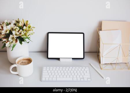 Digital tablet mockup with pen, keyboard, cup of coffee, paper notebooks, flowers on home office desk table. Stylish feminine workspace. Minimal style Stock Photo