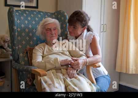woman (daughter) showing kindness to very old lady in care home Stock Photo