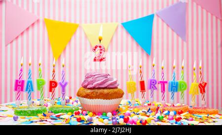 Happy birthday. On a pink background, a happy birthday greeting for a child. Cupcakes with pink cream with a burning candle. Copy space. Stock Photo