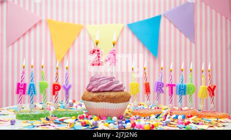 Happy birthday. On a pink background, a happy birthday greeting for a child. Cupcakes with pink cream with a burning candle. Copy space. Stock Photo