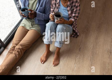 High angle low section of african american young couple with coffee mugs sitting on floor at home Stock Photo