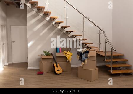 Stack of cardboard boxes with guitar, books and clothing by staircase in new empty house, copy space Stock Photo