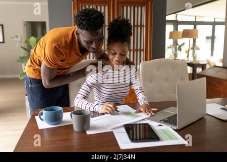 African american young man assisting girlfriend analyzing bills by laptop on table at home Stock Photo