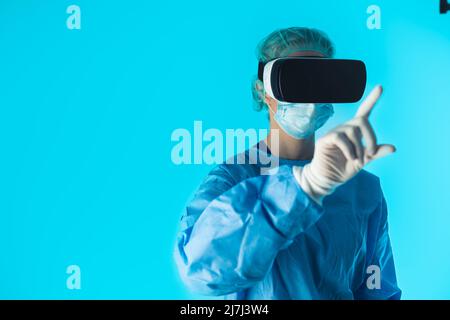 Studio shot of a surgical female doctor wearing a surgeon's outfit with vr goggles on her head touching something with her finger. High quality photo Stock Photo