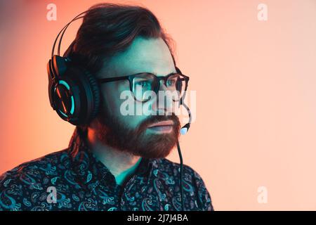 Focused dark-haired millennial man wearing a shirt and eyeglasses using a mic attached to big black headphones. Studio shot. High quality photo Stock Photo