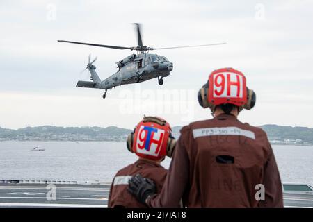 220508-N-BR419-1058 TOKYO BAY, Japan (May 8, 2022) Aviation Structural Mechanic Airman Gregory Blandon, left, from Los Angeles, and Aviation Electrician’s Mate 3rd Class Alexander Dimmick, from Lapeer, Michigan, prepare for an MH-60S Sea Hawk, attached to the Golden Falcons of Helicopter Sea Combat Squadron (HSC) 12, to land on the flight deck of the U.S. Navy’s only forward-deployed aircraft carrier USS Ronald Reagan (CVN 76). Ronald Reagan, the flagship of Carrier Strike Group 5, provides a combat-ready force that protects and defends the United States, and supports alliances, partnerships a Stock Photo