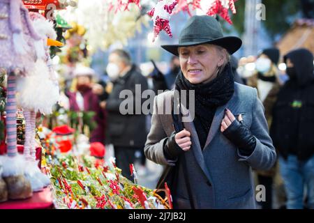 Positive elderly woman in festive mood walking on street Christmas fair Stock Photo