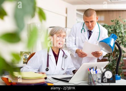 Two physicians working with case histories on laptop in office Stock Photo