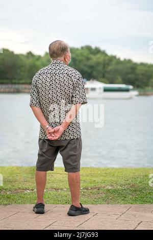 Rear view of senior asian man looking out at a lake horizon. Travel or vacation concept. Stock Photo