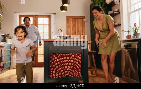 Playful parents chasing after their son in the kitchen. Happy young family having fun together during playtime. Mom and dad spending some quality time Stock Photo