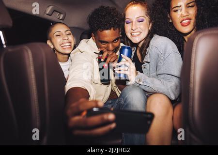 Friends taking a selfie inside a car at night. Group of happy young friends smiling cheerfully while posing for a group photo. Carefree friends taking Stock Photo