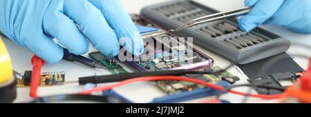Foreman in rubber gloves repairing mobile phone with tweezers in workshop closeup Stock Photo