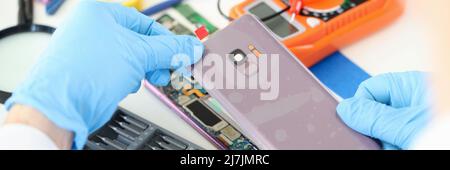 Craftsman in rubber gloves closing cover of mobile phone in workshop closeup Stock Photo