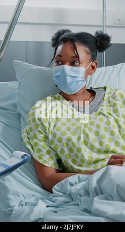 Medical specialist doing healthcare checkup with sick woman in bed during coronavirus pandemic. Physician taking notes and having conversation with patient, wearing face masks. Stock Photo