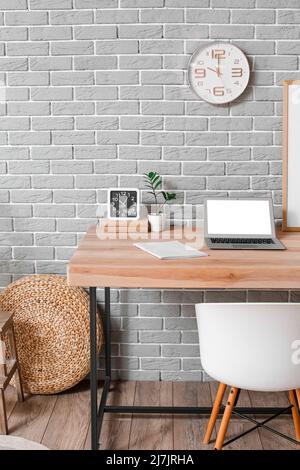 Modern laptop, notebook and alarm clock on wooden standing desk near grey brick wall Stock Photo