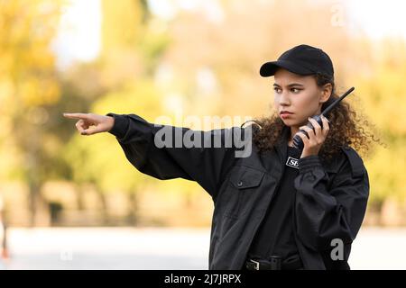 African-American female security guard with radio transmitter pointing at something outdoors Stock Photo