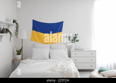 Flag of Ukraine hanging on light wall in modern bedroom with houseplants Stock Photo