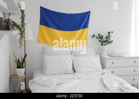 Flag of Ukraine hanging on light wall in modern bedroom with houseplants Stock Photo