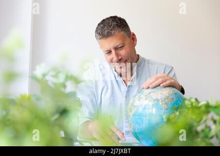Business portrait of environmental engineer, ecologist, garden architect sitting at his work table holding a globe in his hands and surrounded by plan Stock Photo