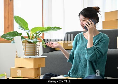 Charming millennial woman works in her living room and receives a good call from her supplier. SME small business startup, e-commerce business. Stock Photo