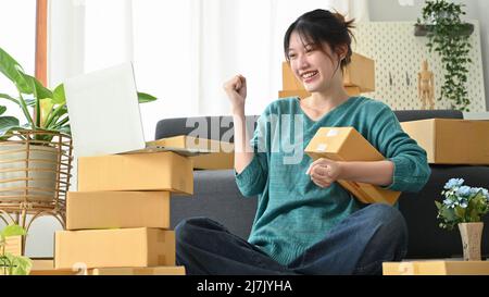 Success Asian female freelancer working at home, Confident female online business shop owner satisfied with her business turnover, raising hand with p Stock Photo