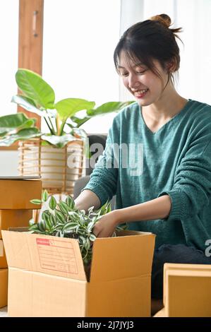 Portrait of a female small online business owner packing her small indoor plants in a parcel box, ready to ship to customers. SME business startup. Stock Photo