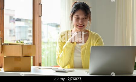 Smart and successful Asian young online seller using laptop computer, planning her online strategy for her business. E-commerce business concept Stock Photo